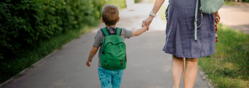 Young child with a green backpack holding hands with his mother